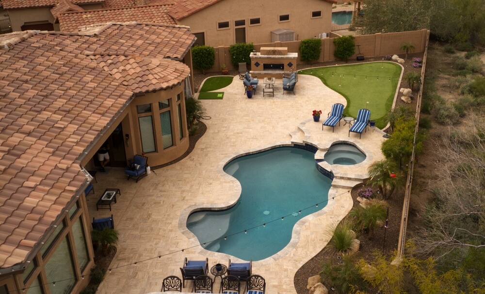 Aerial view of a freeform pool with an attached spa and a travertine deck in a spacious backyard